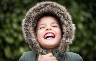 Child in Green Jacket Smiling after pain-free silver diamine fluoride cavity treatment
